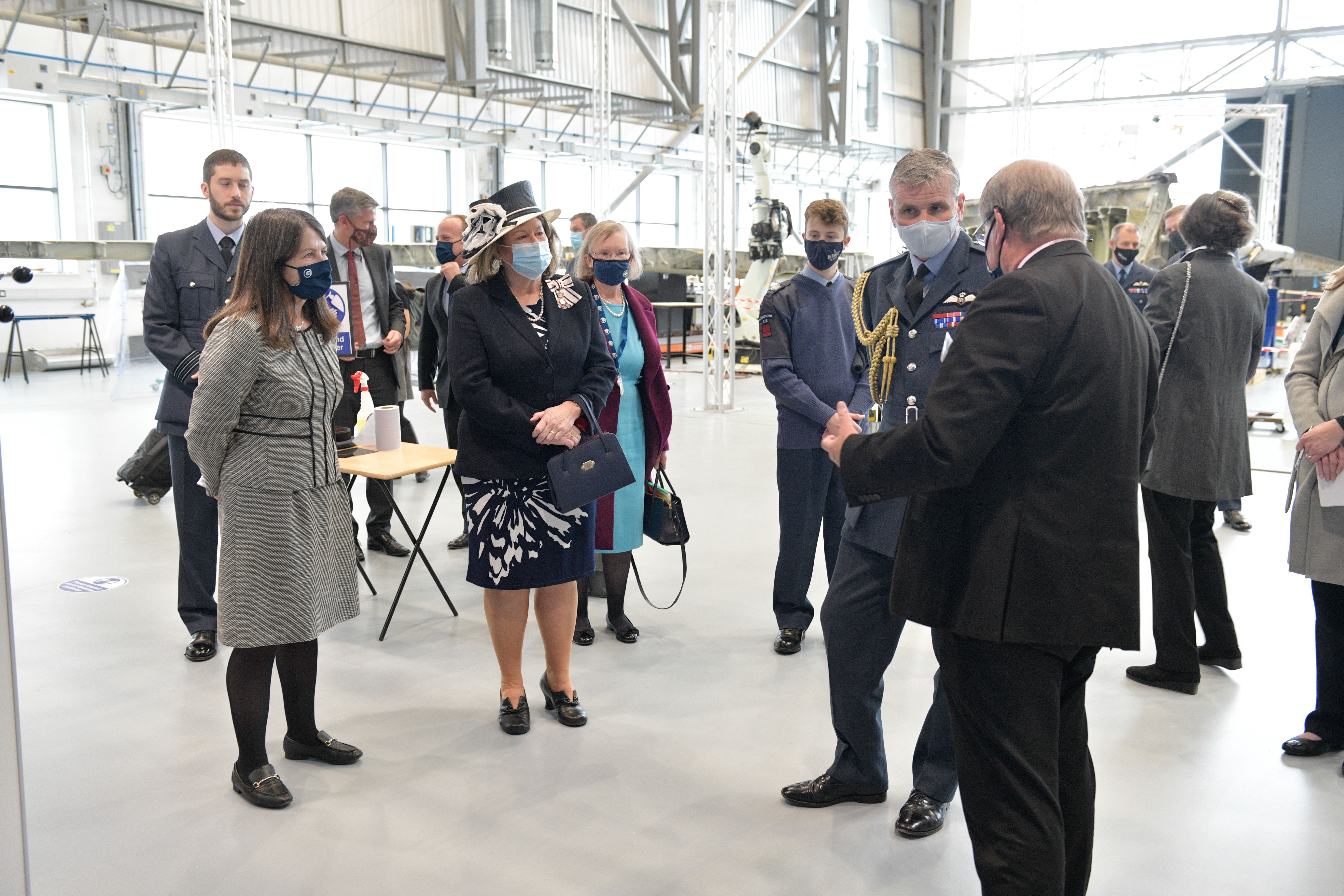 Personnel and significant individuals stand inside a hangar.